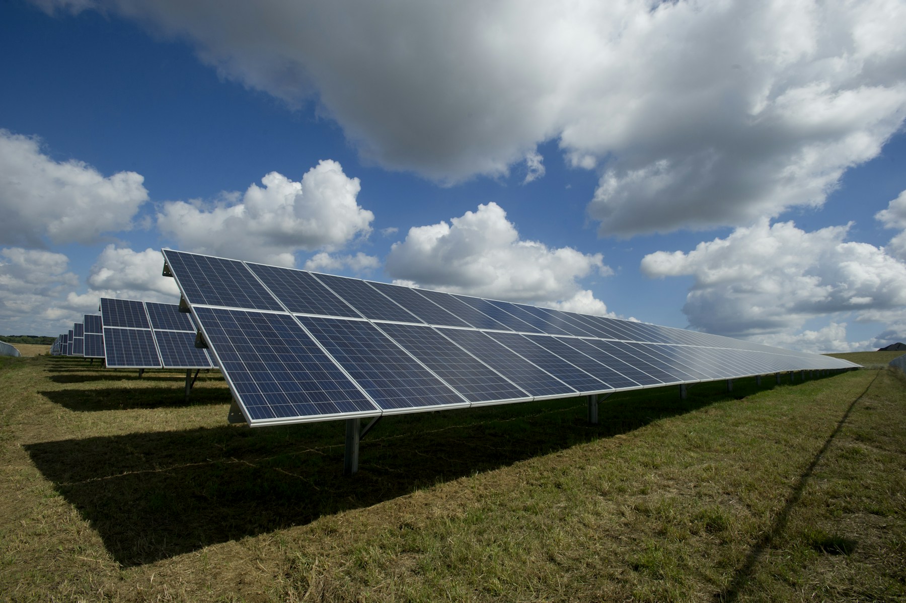 Rows of solar panels beneath a cloud-filled blue sky